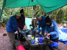 Lori watches Dan, Steve, and Jo Ann ply
                       their craft in a backpacker's kitchen