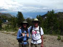 Lori and David pose in front of a forest fire in the background, as well as a decrepit gondola to the microwave relay station above