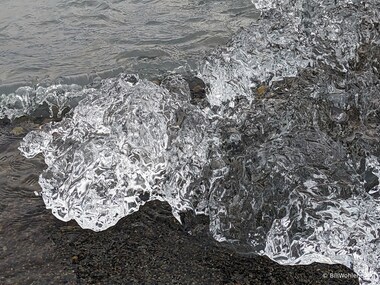 A chunk of glacial ice that has washed up on the beach glimmers as waves wash across it